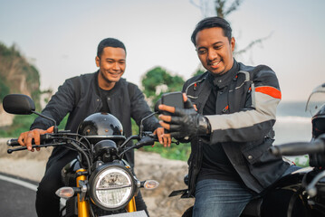 asian motorcyclist holding phone and watching it together with his friend