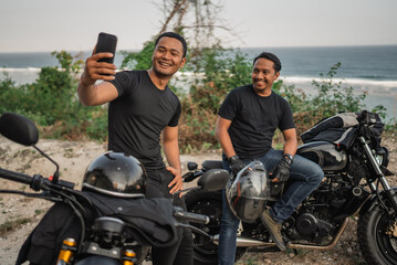 asian men sitting on motorbike and taking picture together using handphone
