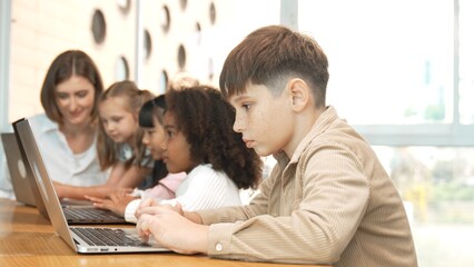 Boy playing laptop with multicultural friend learning prompt at STEM technology class....