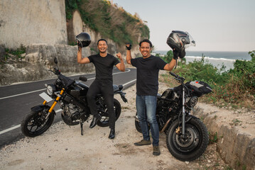 asian male riders standing beside motorcycle lifting helmet
