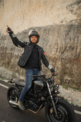 asian man standing while riding motorcycle with open arm gesture
