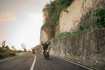 asian rider doing hand off steering while riding motorbike with open arms gesture