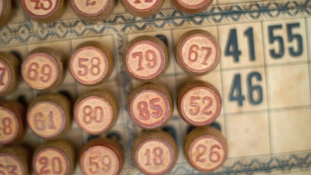 Cinematic close-up smooth pan left, shot from above of a Bingo wooden barrels, woody figures, old numbers background, vintage board game, lucky number, professional lighting, slow motion 120 fps