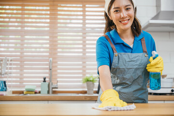 Asian woman in yellow gloves performs housekeeping cleaning kitchen counter with liquid spray....
