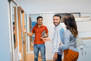 male store clerk with gestures offering wooden wardrobe products to customers at a furniture store