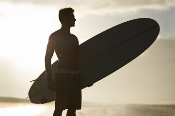 Surfing, sunset and silhouette of man at a beach with surfboard for freedom, travel or sports...