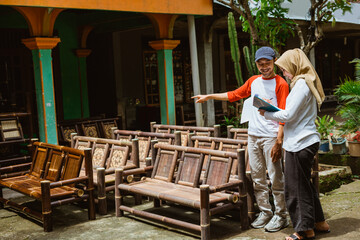 Asian man and woman in hijab bamboo chair handicraft businessman checking goods outside the house