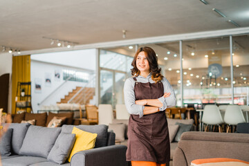 attractive woman in apron with crossed arms standing in front of couch in furniture store department
