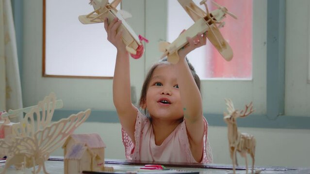 Asian girl is coloring and playing with assembly wooden airplane toy