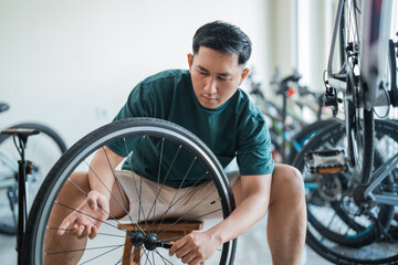 young Asian man installs axles while working in a bicycle shop - obrazy, fototapety, plakaty