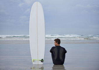Beach, fitness and man thinking with a surfboard for wellness, sports and training while sitting in...