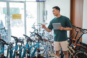 young man counts the number of new bicycles while using a tablet at a bicycle shop