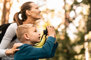 Mother child together hiking in the forest looking through binoculars bird watching exploring learning about nature, family adventure 