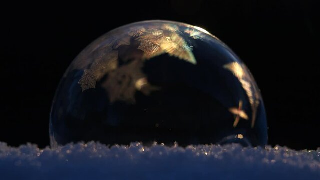 Soap bubble on snow freezing in cold winter weather on black background