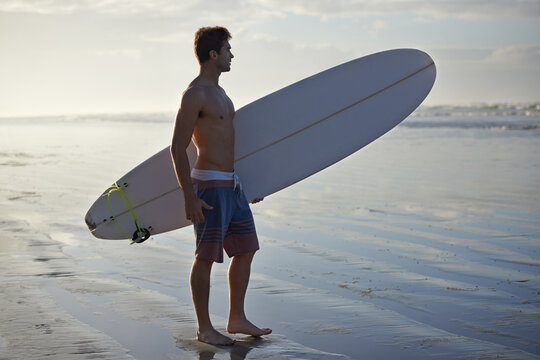 Man, beach and surfboard for waves, exercise or outdoor hobby in fitness, surfing or practice. Male person or surfer with long board for training, seaside or morning by water or ocean coast in nature
