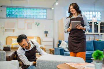 female shop clerk uses a tablet while a male clerk adjusts the chairs in a furniture store