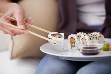 Hands, sushi plate and chopsticks in home, closeup or eating for wellness, diet or meal with soy...