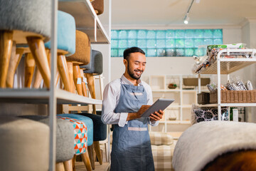 shopkeeper man in apron using a tablet while standing in a furniture store
