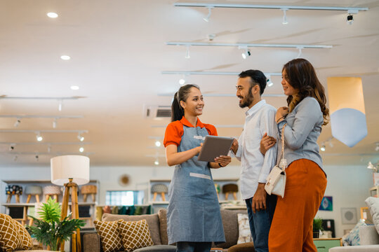 Female shop assistant holding a tablet while chatting with a married customer at a furniture store