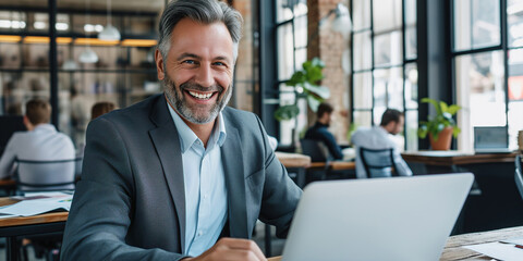 Mature businessman with grey hair and beard using laptop in office