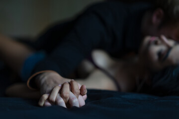 Man's hand holding a woman hand for rape and sexual abuse concept. Couple in love holding hands tight in bed close-up touching each other on a black blanket, enjoying honeymoon, valentine's day - obrazy, fototapety, plakaty