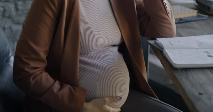Tilt-up portrait of ambitious pregnant lady speaking on mobile phone discussing business in office. Professional communication and pregnancy concept.