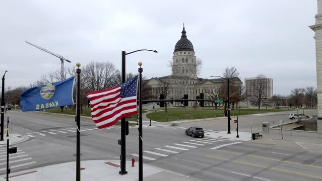 Kansas state capitol building with flags waving in wind in Topeka, Kansas with drone video moving up.