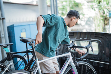 young man locking bike while holding bike on pickup car with bike shop in background