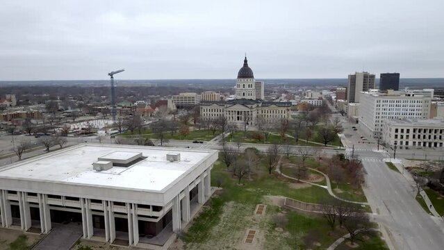 Kansas state capitol building with flags waving in wind in Topeka, Kansas with drone video circling wide shot.