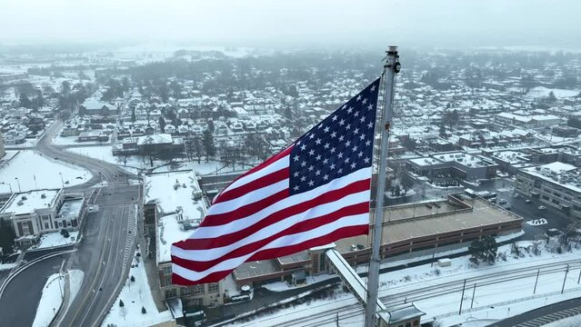Aerial close up of American flag waving over snowy suburban landscape. Small town USA theme.