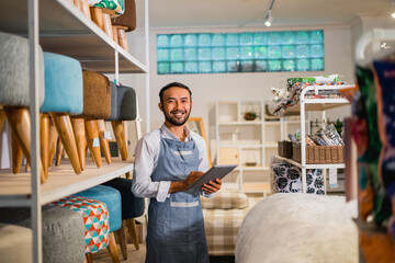 male shopkeeper smiling looking at camera while using a tablet in furniture store