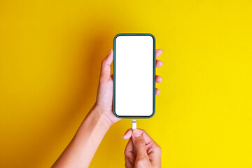 Woman's hand plug in micro usb cable into blank white screen smartphone to charge battery isolated on yellow background