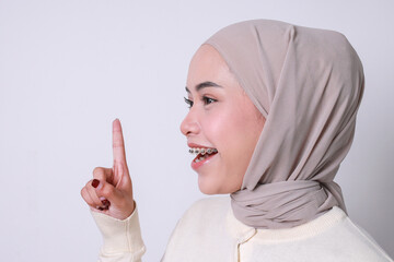 Side view Asian girl with hijab and dental braces pointing up showing copy space or got an idea...