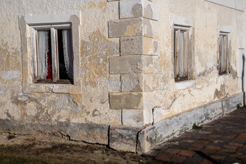 View of a corner of an old, weathered house with windows, the plaster is crumbling from the facade