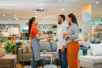 Asian couple buying a sofa. Shop assistants shake hands with customers when buying a sofa at a furniture store - obrazy, fototapety, plakaty