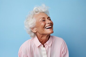 Portrait of cheerful senior woman with white hair laughing against blue background