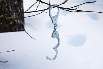 Handcuffs hanging on a branch against the background of footprints in the snow, the concept of...