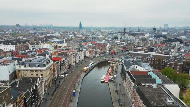 The drone is flying forward above Rokin canal and street with an overlook of the city centre on a cloudy day in Amsterdam The Netherlands Aerial Footage 4K