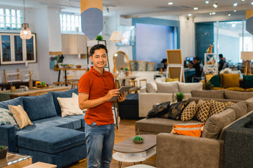 handsome male shop owner smiling using a tablet while standing in furniture store