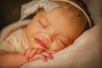 Portrait of a newborn baby. The child smiles. A newborn baby sleeps sweetly in a wooden vintage stroller. Baby girl in a vintage dress with a bow on her head. A little girl lies on her tummy. Small