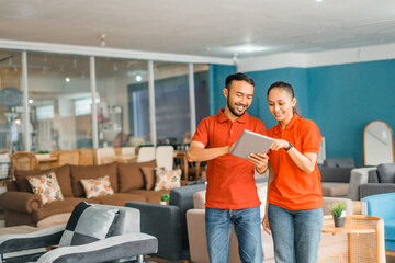 smiling couple in red using a tab standing in front of couch in furniture store department