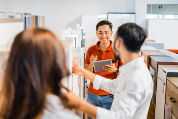 male shop assistant offering a new type of cupboard to husband and wife while shopping at a...