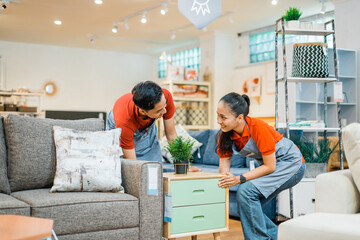 two shop assistants work together to move a small cabinet next to a sofa at a furniture store