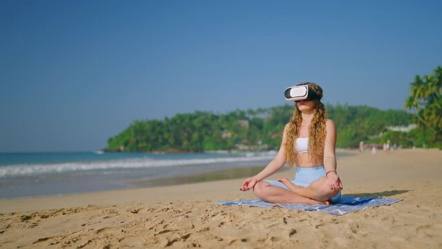 Woman meditates with VR headset on tropical beach. Virtual retreat, practices mindfulness, seated in lotus pose, tranquil ocean backdrop. Relaxing in virtual reality, immersive calmness experience.