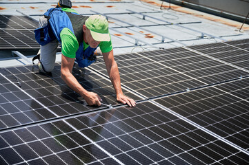 Worker building photovoltaic solar panel system on rooftop of house. Man engineer installing solar...