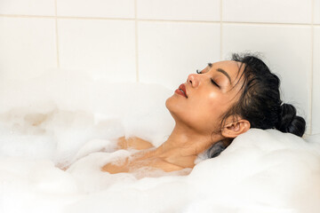 Young woman lying in a bathtub with foam