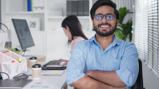 Portrait of formal business man confident successful. Indian businessman or manager in light blue shirt, stands at workplace in office, arms crossed, looks directly at camera and smiles friendly