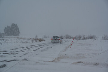 Car traveling through bad weather with blowing snow over fields