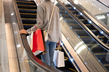Cropped image of a woman with shopping bags is going up an escalator in a shopping mall.