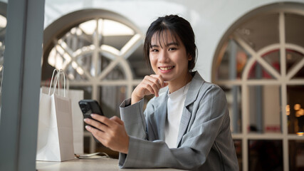 Charming Asian woman in trendy clothed is using her smartphone while relaxing in a cafe in the city.